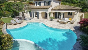 A large swimming pool with a curved edge, surrounded by a patio area with lounge chairs and a covered seating area.