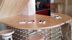 Un'area pranzo in legno con un tavolo rotondo e sgabelli, una cucina sullo sfondo e un soffitto a falde.