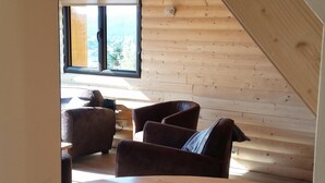 Una stanza accogliente con pareti e soffitto in legno, una finestra con vista, un tavolo di legno con un vassoio e un divano in pelle marrone.