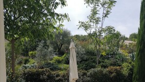 An outdoor patio with a table set for four, surrounded by chairs, a table umbrella, and a bottle of wine. - Gîte Néflier (Vogüé)
