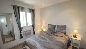 A bedroom with a large bed, two bedside tables with lamps, a mirror, and a window with curtains. - Gîte Néflier (Vogüé)