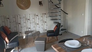 A modern living room with a spiral staircase, a round woven wall hanging, and a dining area with a wooden table set for four. - Gîte Néflier (Vogüé)