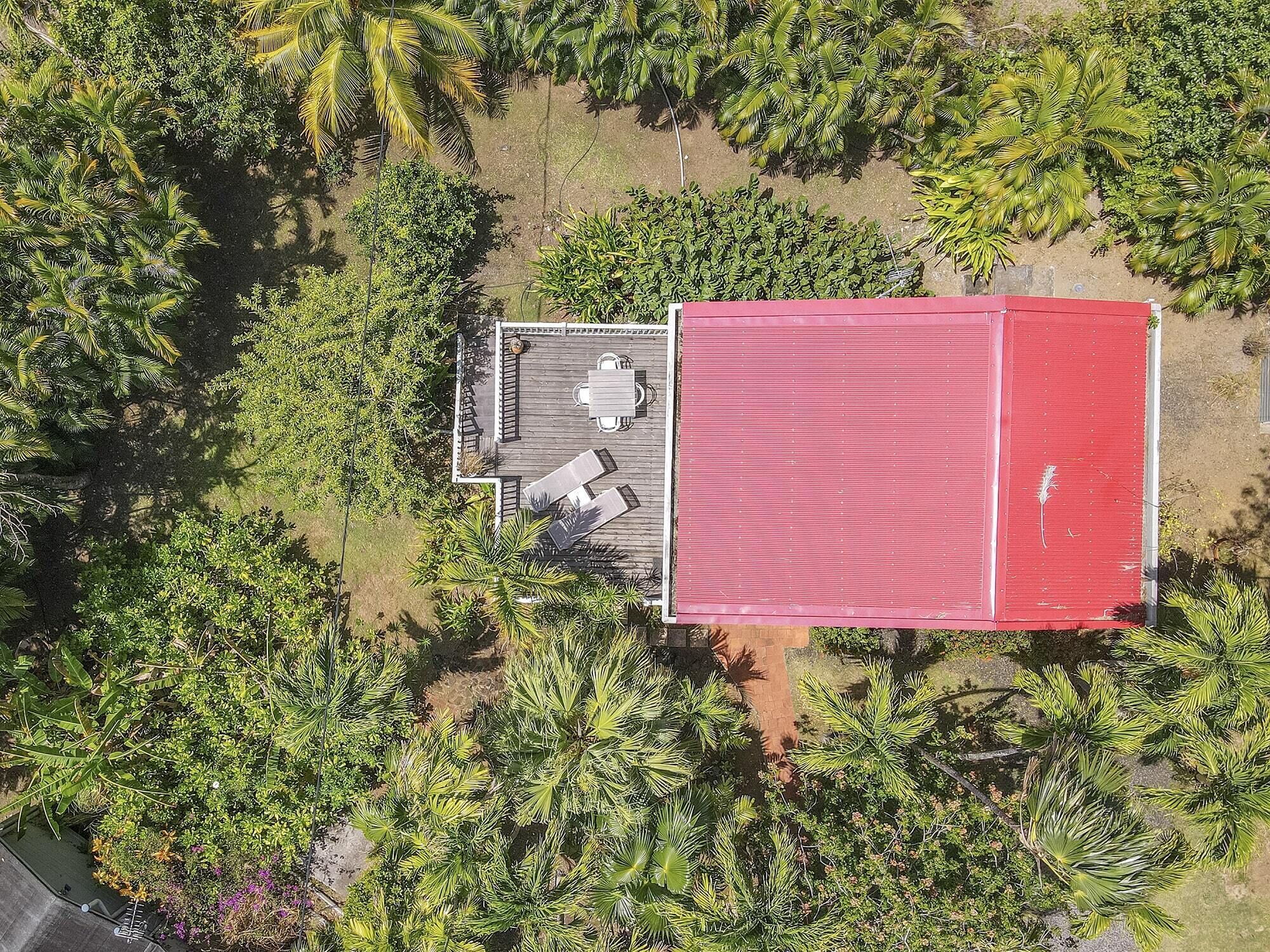 Vista aérea de uma propriedade com um edifício vermelho, um espaço de pátio com mesa e cadeiras, e vegetação ao redor.