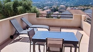 A balcony with a table and chairs, a sunshade, and a view of a town and mountains.