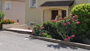A residential building with a tiled roof, a small porch, and a garden with pink flowers.