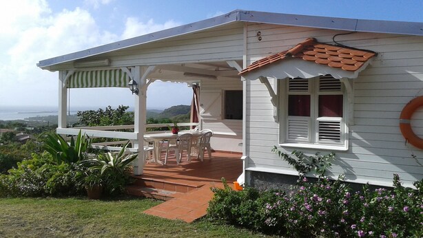 A white house with a covered patio, a view of the ocean, and a lifebuoy on the wall.