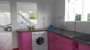 A kitchen with a washing machine, a window with a view, and a sink with a dish soap bottle.