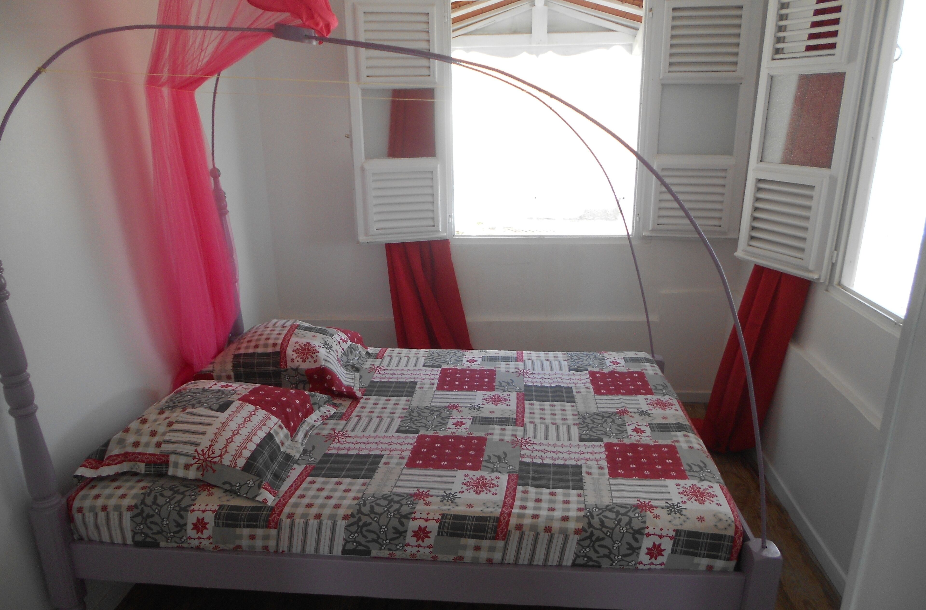 A bed with a quilt, a window with shutters, and a mosquito net.