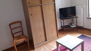 A room with a wooden wardrobe, a television on a stand, a chair, and a small table. - Accommodation 4 people garden, quiet, GERARDMER FREE WIFI (Gérardmer)