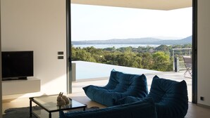 Ein modernes Wohnzimmer mit großem Fenster, einem Flachbildfernseher und einer Sitzecke mit blauen Kissen.