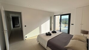 Ein Schlafzimmer mit Bett, Blick durch eine Schiebetür auf einen Balkon und einem Flur, der zu einem weiteren Zimmer führt.