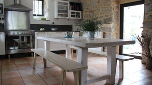 Een keuken met een houten tafel, bankjes, een fornuis, kastjes en een potplant.