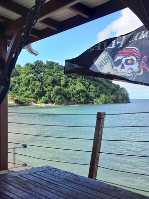 Una hamaca y una bandera con diseño de calavera, con vistas al mar azul cristalino y una isla boscosa.
