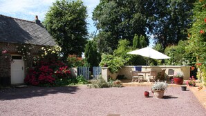 A garden with a gravel patio, a white umbrella, and potted plants.