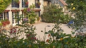 A traditional stone building with a courtyard, surrounded by lush greenery and flowering plants.