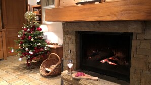 A cozy living room with a stone fireplace, a Christmas tree, and a wicker chair. - Cosy chalet with outdoor spa and sauna facing Mont Blanc - MontchavinLa Plagne (La Plagne Tarentaise)