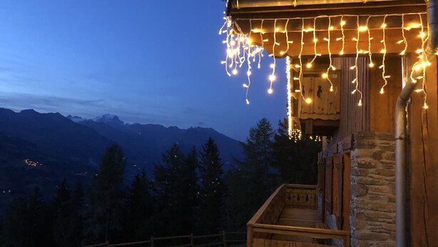 A wooden building with a stone wall, a wooden deck, and a view of mountains in the background. - Cosy chalet with outdoor spa and sauna facing Mont Blanc - MontchavinLa Plagne (La Plagne Tarentaise)