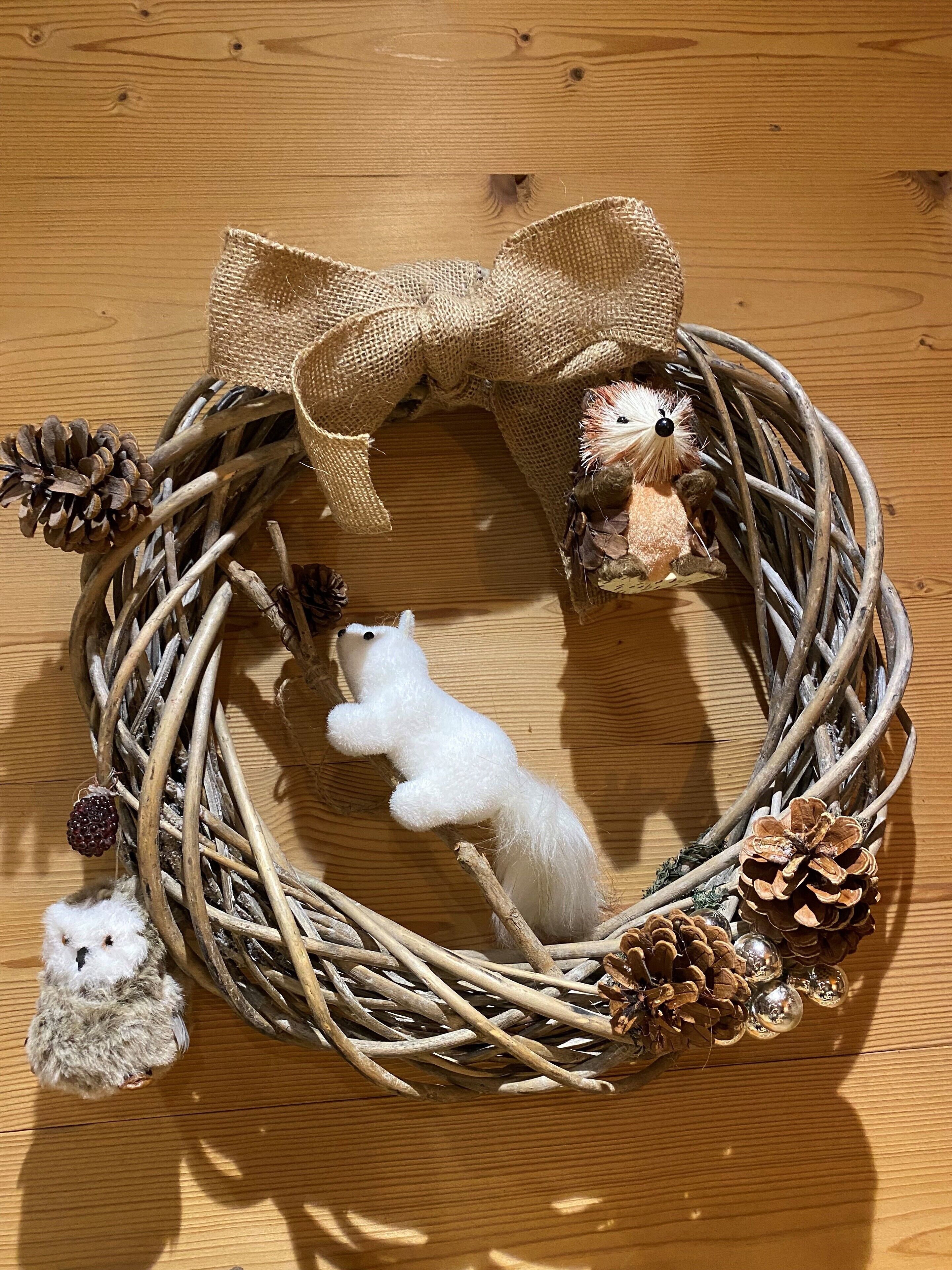 A wooden surface with a decorative wreath featuring a bow, pinecones, and small plush toys.
