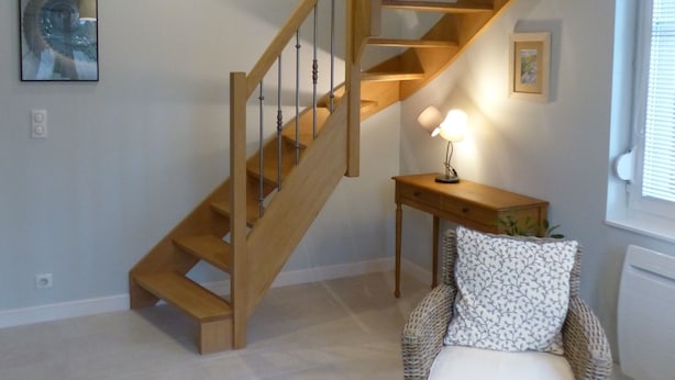A modern interior with a wooden staircase, a wicker chair with a cushion, and a small table with a lamp.