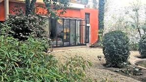Un bâtiment moderne doté d’une véranda en verre, entouré d’une végétation luxuriante et bordé d’un chemin de gravier.