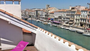 Un balcon avec deux chaises longues roses donnant sur une marina où l’on peut admirer des bateaux et des bâtiments.