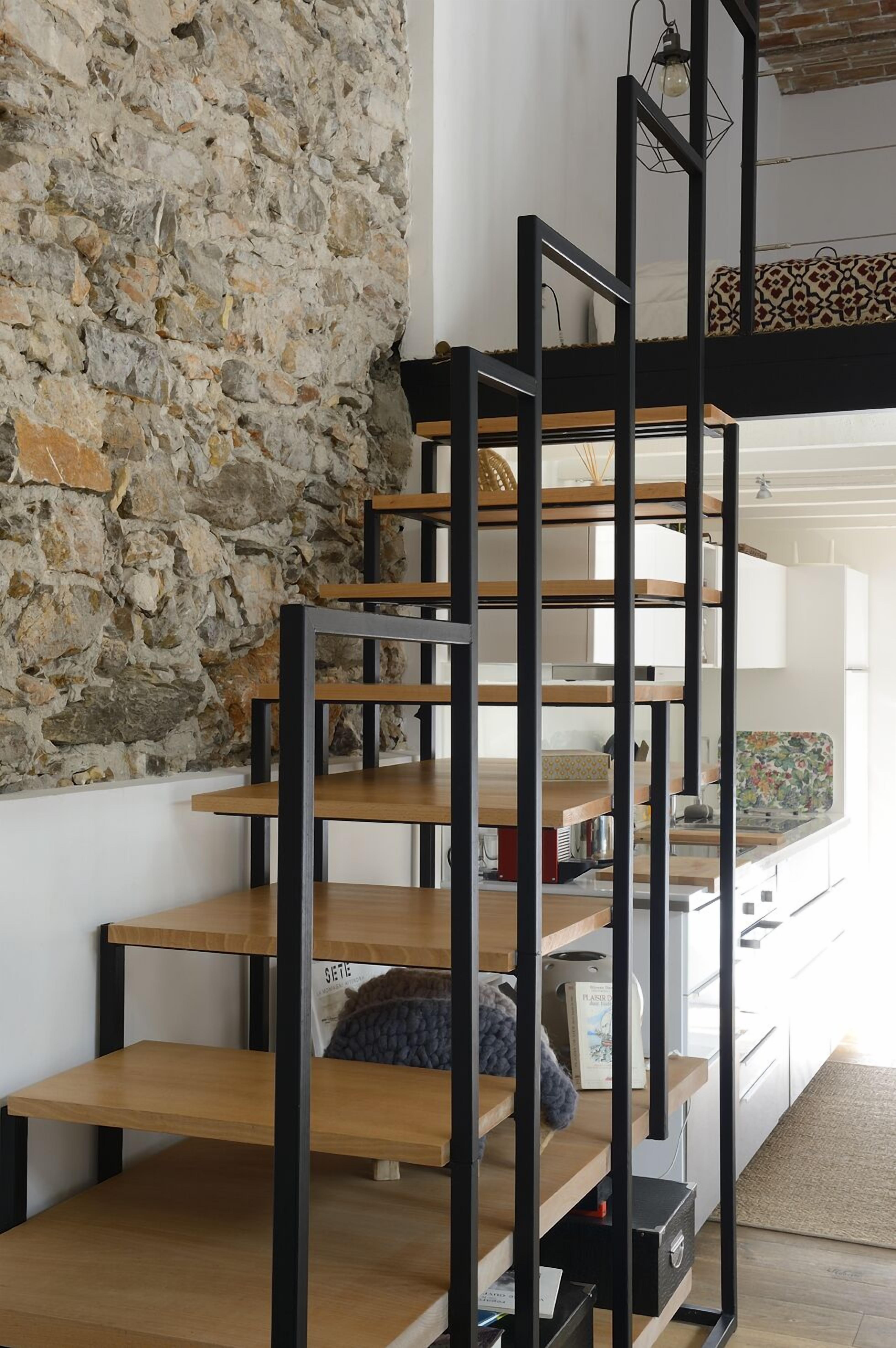 Ein modernes Interieur mit einer Steinsäule, einer schwarzen Metalltreppe und einer Holzplattform.