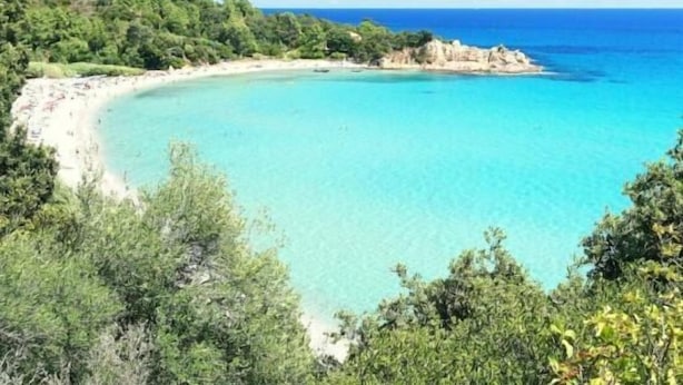 Un paysage côtier caractérisé par une mer turquoise aux eaux limpides, une plage de sable et une végétation luxuriante.