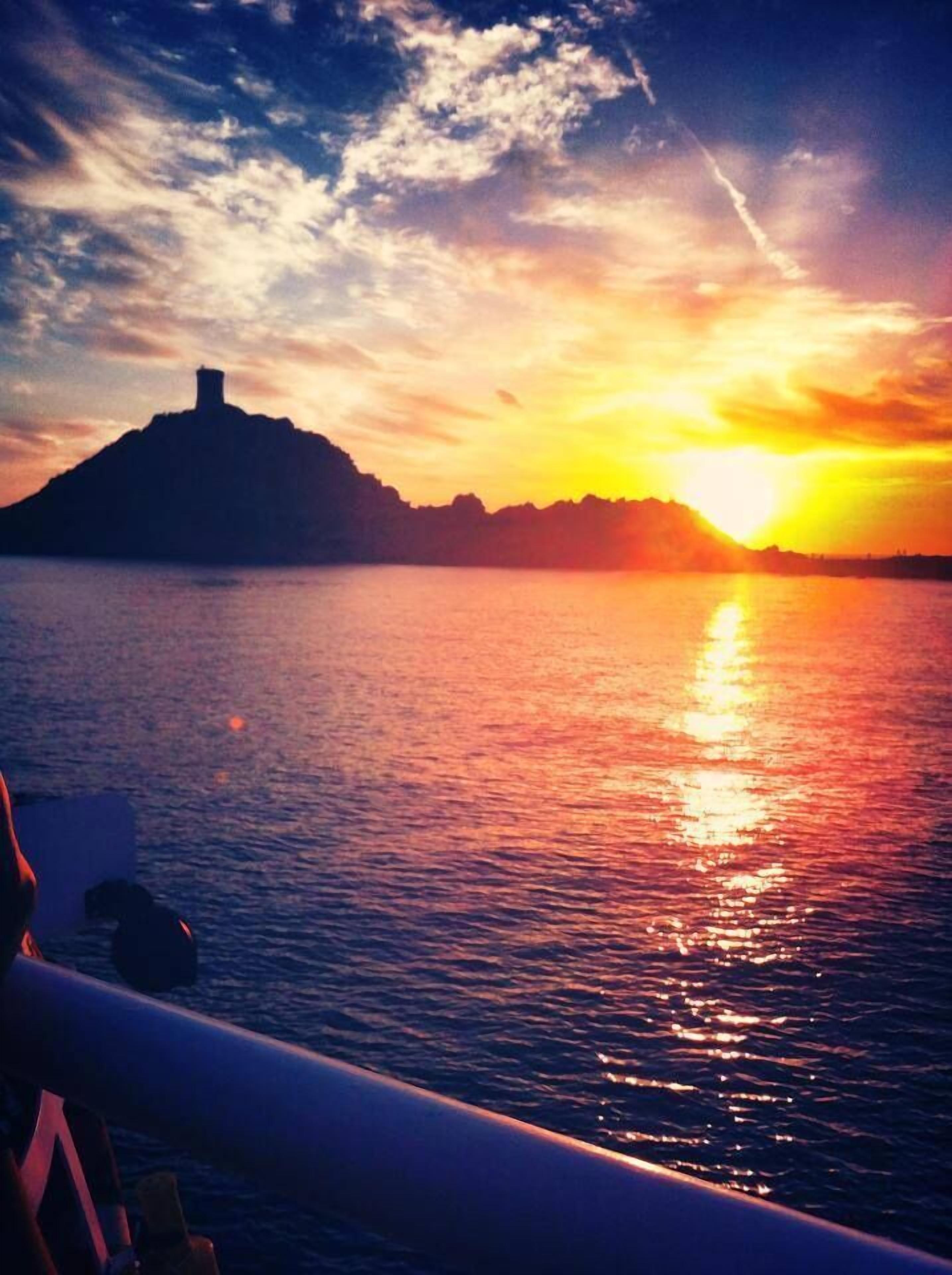 A sunset over water with a silhouette of a hill and a tower.