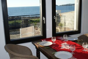 Espaço de jantar com mesa posta para dois, com vista para o litoral.