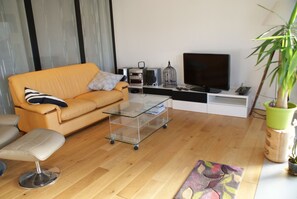 Sala de estar com sofá, mesa de centro de vidro, televisão e planta em vaso.