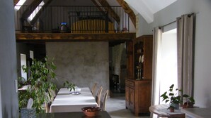 Ein Essbereich mit einem langen Tisch, Stühlen und einer Holzbalkendecke. Es gibt einen Schrank mit Glastüren und einen kleinen Tisch mit einer Pflanze.