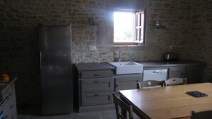 Eine Küche mit Steinwand, einem Fenster, einer Spüle, einem Kühlschrank und einem Holztisch.