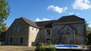 Ein Gebäude aus Stein mit Schwimmbad, das traditionelle Architektur durch ein Satteldach und viele Fenster zeigt.
