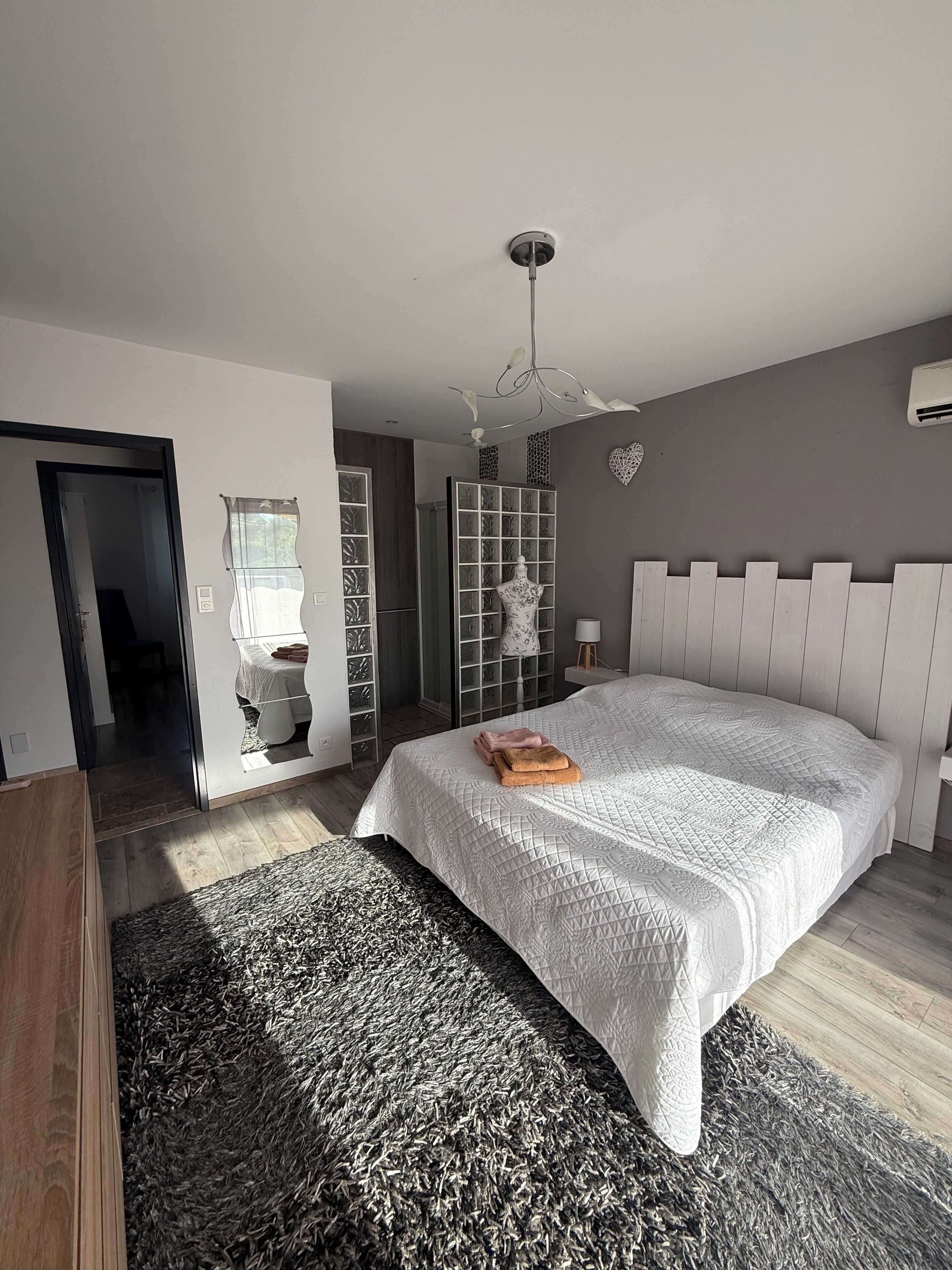 A modern bedroom with a large bed, a wardrobe, a vanity, and a bathroom visible through an open door.
