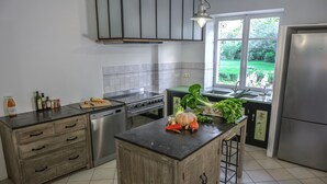Een moderne keuken met een centraal eiland, roestvrijstalen apparatuur en uitzicht op een tuin door het raam.
