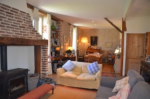 A cozy living room with a fireplace, a sofa, a dining area, and a kitchen visible in the background. - 🌿Havre de Paix pour 2-3 Familles - Between Penne-d'Agenais and Tournon-d'Agenais (Trémons)