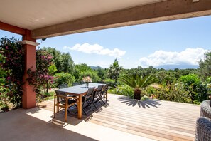 A wooden deck with a table and chairs, surrounded by lush greenery and a clear view of the landscape. - 10 minutes walk from the beach of Saint Cyprien, by trails. (Zonza)