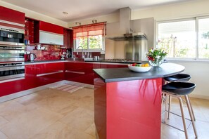 A modern kitchen with red cabinetry, stainless steel appliances, and a central island with stools. - 10 minutes walk from the beach of Saint Cyprien, by trails. (Zonza)