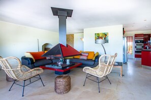 A modern living room with a sofa, two wicker chairs, a coffee table, and a fireplace. - 10 minutes walk from the beach of Saint Cyprien, by trails. (Zonza)