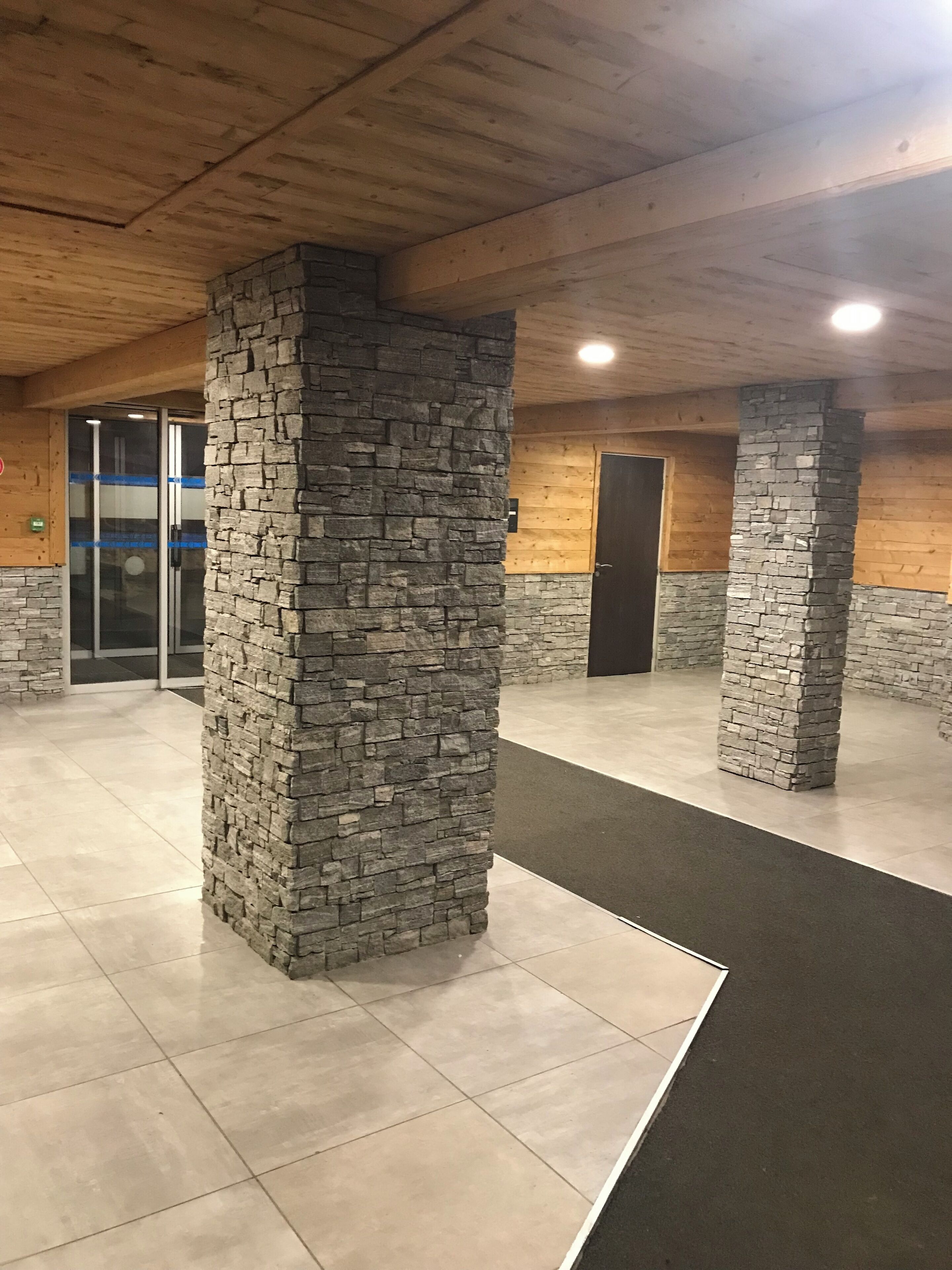 A spacious lobby with stone pillars, a tiled floor, and a wooden ceiling.