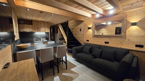Un intérieur moderne avec un plafond en bois, un coin cuisine, un espace repas avec des chaises, un canapé et un escalier.