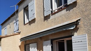 Ein zweistöckiges Gebäude mit einer Terrassenfläche, die einen Tisch, Stühle, einen grünen Wasserkrug und eine Steckdose zeigt.