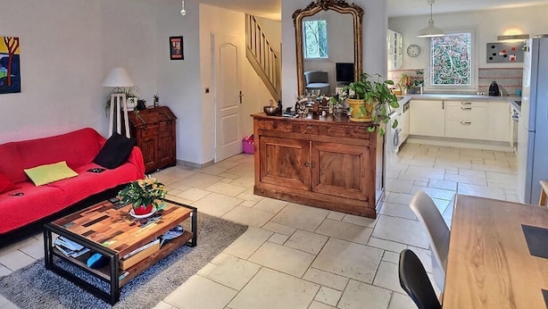 Ein Wohnzimmer mit rotem Sofa, einem Holztisch und einer Küchenzeile mit weißen Schränken und einem großen Spiegel.