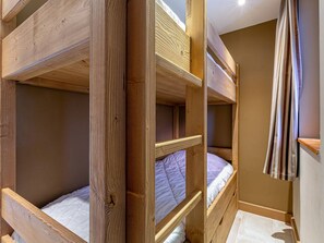 Een slaapkamer met een stapelbed, houten constructie, een gordijn en een betegelde vloer.