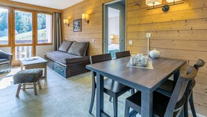 Una habitación acogedora con detalles de madera, un sofá, una mesa de comedor con sillas y un taburete pequeño.