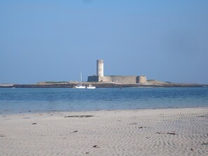 En sandstrand med en historisk stengrund og en lille båd i vandet.