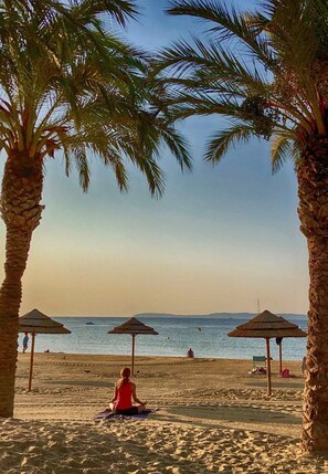 Une scène de plage avec des palmiers, des parasols de plage et une personne en méditation.
