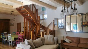 Amplia sala de estar con escalera de madera, sofá de cuero marrón, mesa de centro de madera y zona de comedor con sillas coloridas.