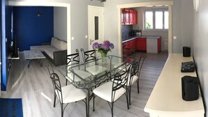 Eine moderne Küche mit roten Schränken, ein Essbereich mit einem Glastisch und Metallstühlen sowie eine Wand in Blautönen.