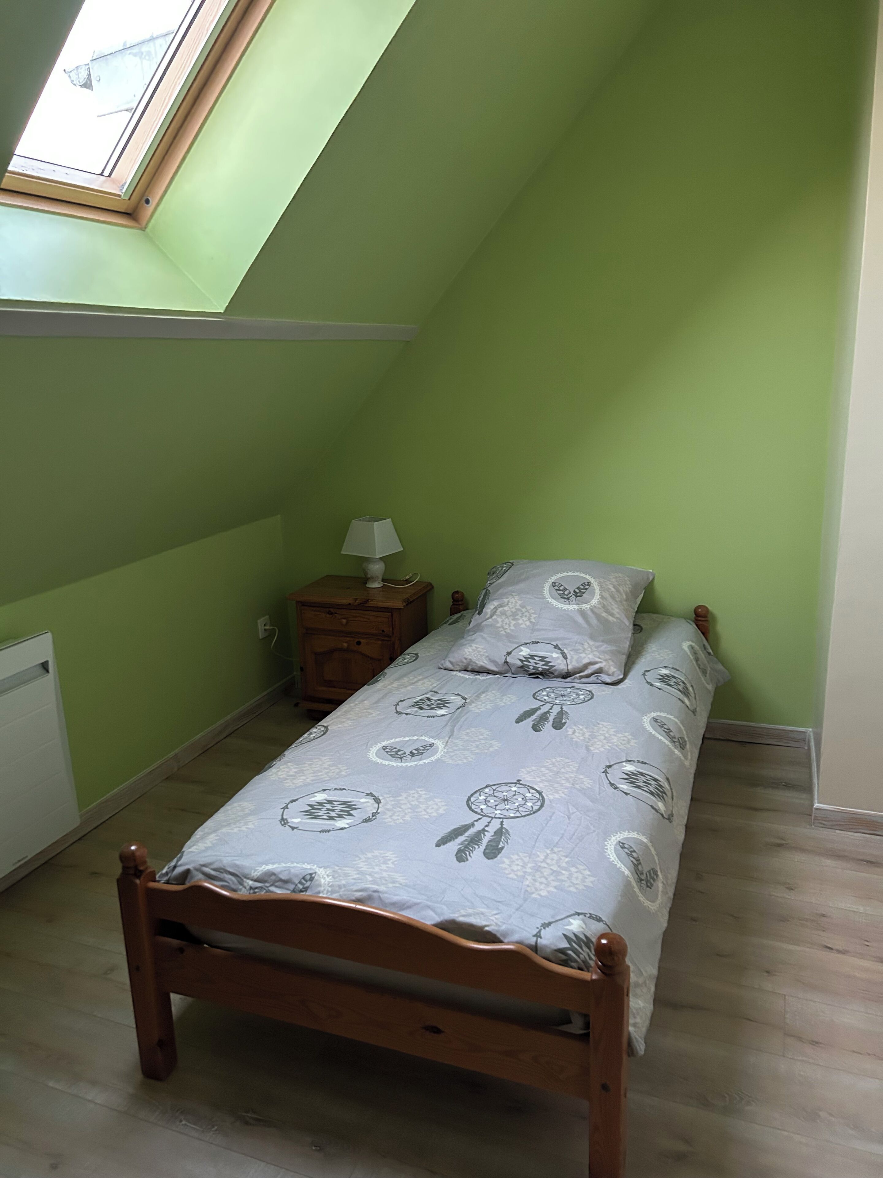 Een kleine kamer met een enkel bed, schuine wand en dakraam.